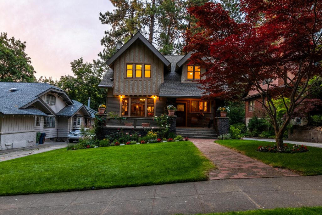 Quaint Victorian-style home with a glowing interior, surrounded by a lush garden at twilight.